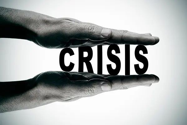 Two hands squeezing the word CRISIS, depicting pressure or stress.