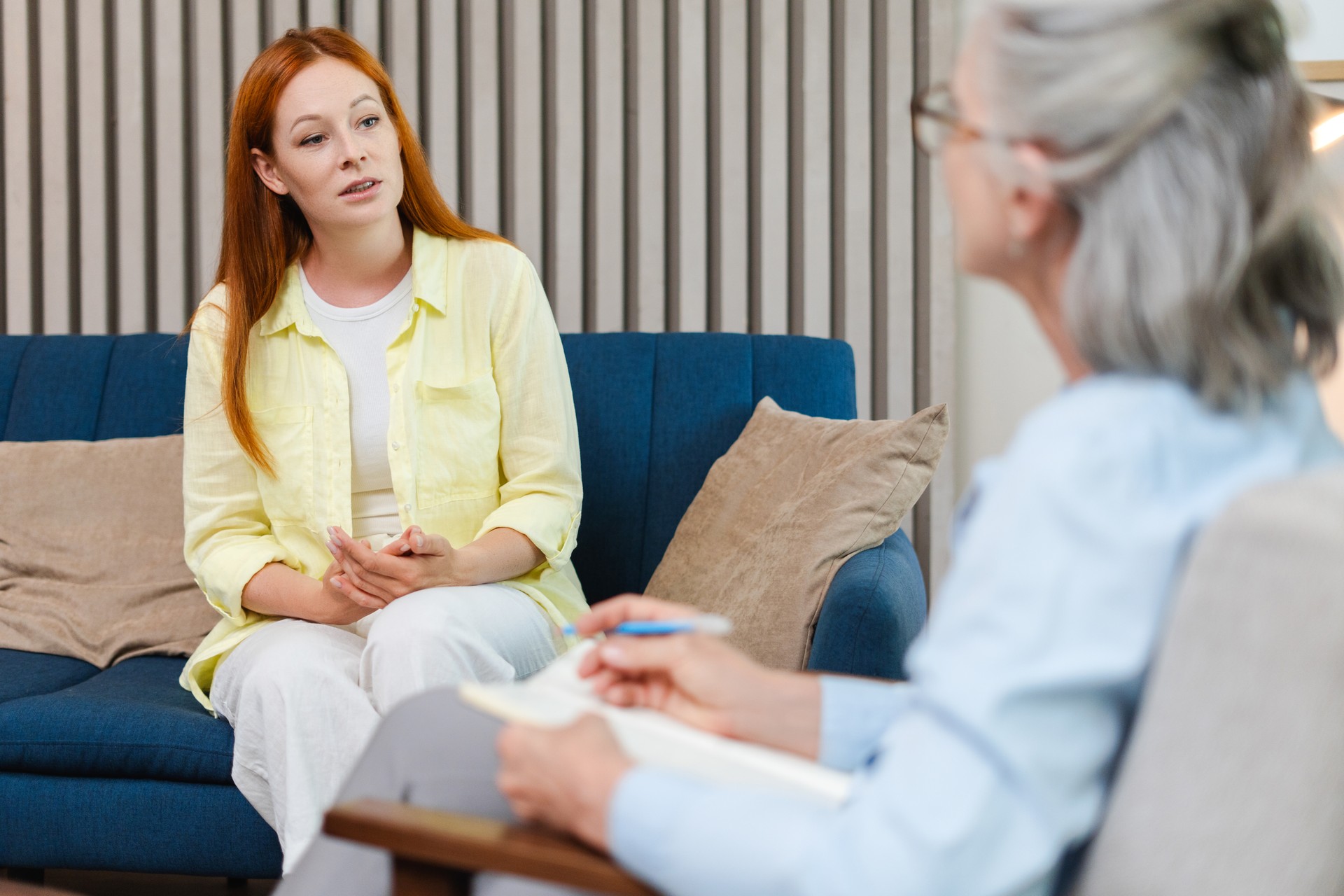 Young woman talking to senior psychologist sitting on sofa during therapy session