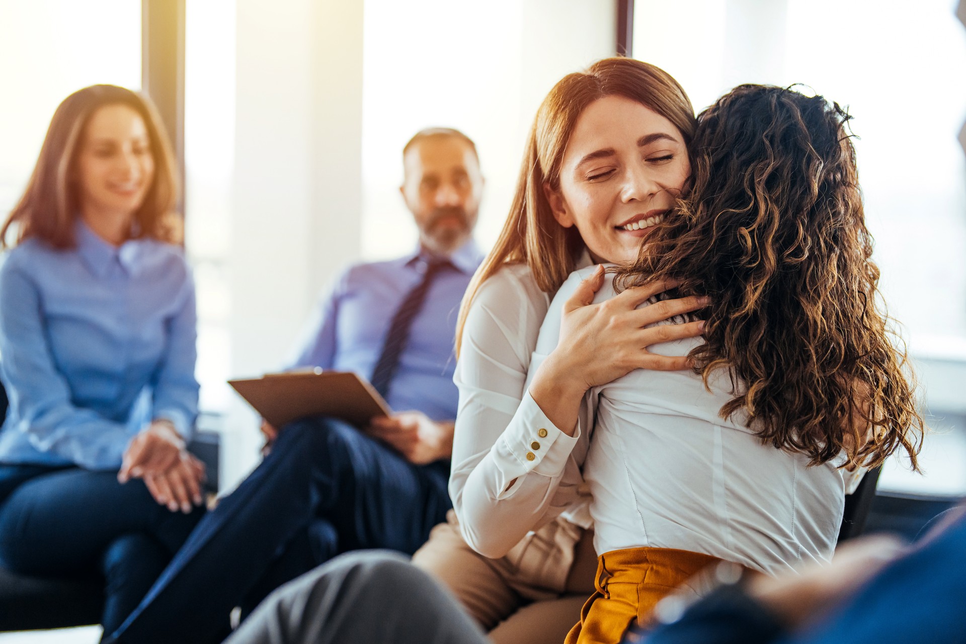 Portrait of female psychologist embracing young woman during therapy session in support group.